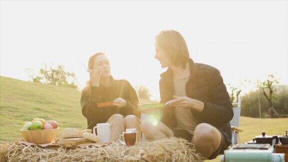 美丽的高加索年轻夫妇享受野餐在日出男人和女人喝咖啡和热茶草原和山脉的背景