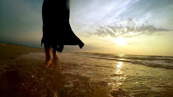 慢镜头:一名女子沿着沙滩行走将水花溅向镜头