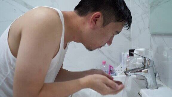 年轻人在浴室水槽上面洗脸