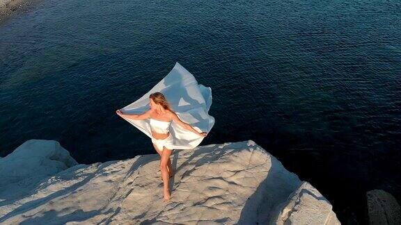 在爱琴海海岸的一块岩石上一个女人拿着一块巨大的白色织物
