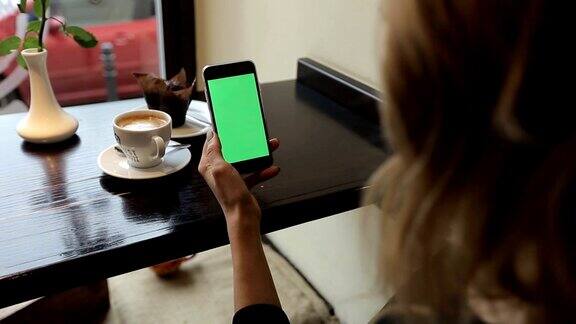 迷人的年轻女子使用她的绿色触摸屏手机在咖啡馆