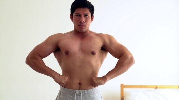年轻的亚洲男子运动躯干显示他的二头肌在他的房间