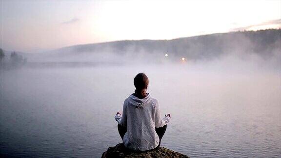 女人在练习瑜伽和莲花体位冥想美丽的雾蒙蒙的日出湖上