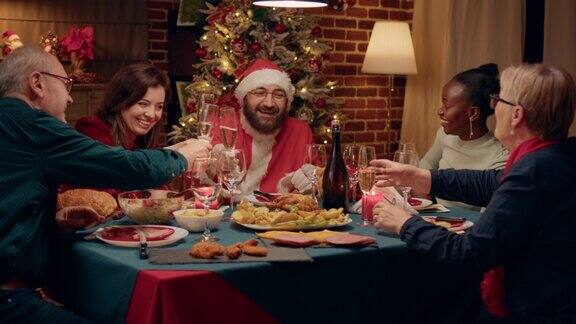 装扮成圣诞老人的快乐男子与家人一起喝香槟享受圣诞晚餐