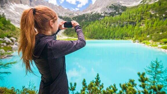女人在山上徒步旅行美丽的湖的惊人的景色虚幻的蓝色与智能手机