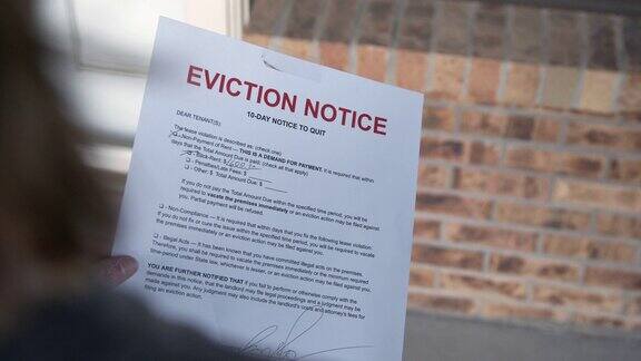 一名女性的白种人手在一所出租房屋的前门上挂着一张纸驱逐令