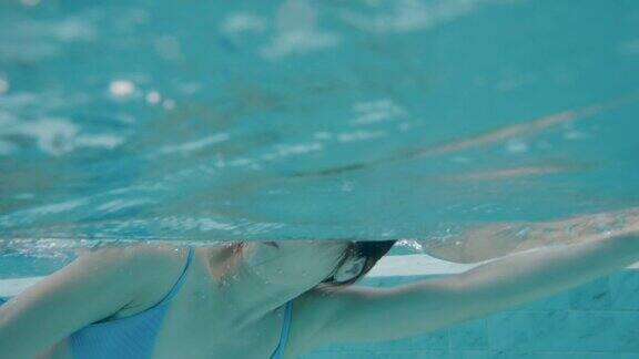 一名身着蓝色泳衣的亚洲美女正在度假时海边的酒店泳池里游泳