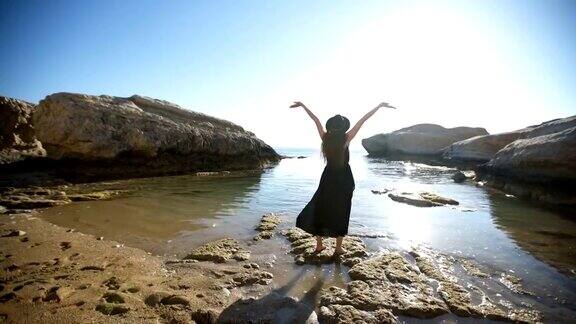 年轻女子在岩石海岸摆姿势张开双臂