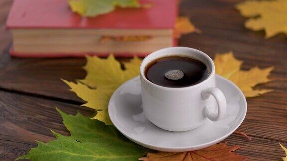 木桌上的咖啡杯上放着书五彩缤纷的秋叶和旋转的咖啡泡沫