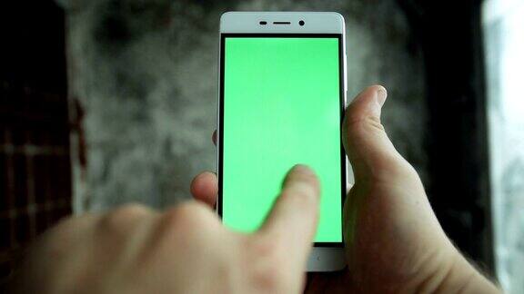 特写男子手持和触摸手机与绿色屏幕垂直