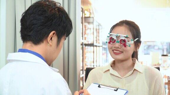 验光师在为亚洲年轻女性的视力测试调整距离试架后写报告准备制作眼镜表达积极的情绪微笑以获得更好的视力