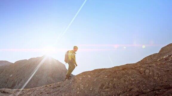 一名男性登山运动员在太阳耀斑中行走在岩石山脊上