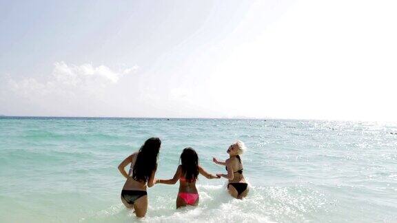 穿着比基尼的女孩们在水里牵着手在海滩上跑后视图快乐的妇女在暑假群游客