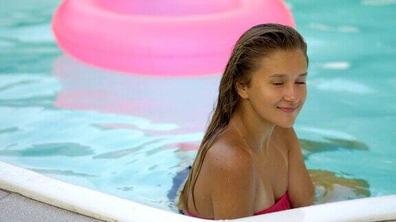 快乐的女孩放松在充气的粉色甜甜圈浮年轻的女人在比基尼享受夏天的假期喝鸡尾酒在粉红色的漂浮在游泳池