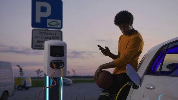 黄昏时分年轻的篮球运动员在停车场给他的电动汽车充电