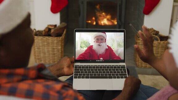 一对戴着圣诞帽的非裔美国夫妇用笔记本电脑进行圣诞视频通话屏幕上有圣诞老人