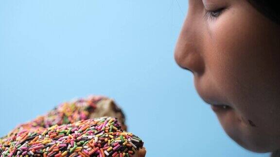 亚洲女孩吃巧克力甜甜圈与蓝色背景侧视图和慢动作