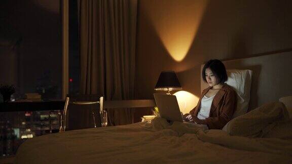 一名年轻的亚洲华人女子晚上在卧室里用笔记本电脑上网