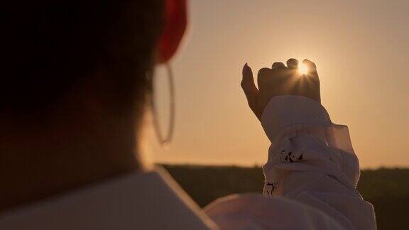 女人在日落时透过手指看太阳手的特写镜头