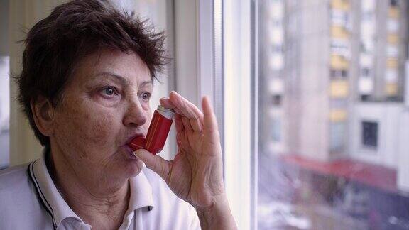 老年妇女一边用哮喘吸入器一边透过窗户往外看
