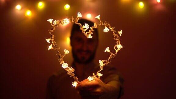 一个男人手里拿着一颗由灯泡做成的心透过它往外看情人节