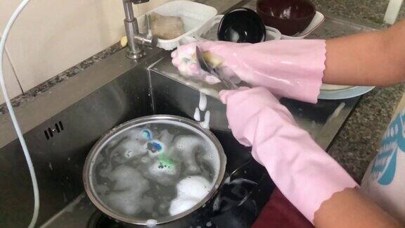 一位戴着手套在家的妇女在水龙头下洗盘子