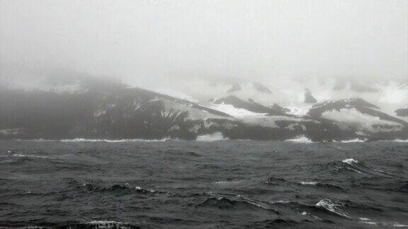 海浪和雾在背景的雪岩石在南极海洋