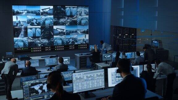 一组在监控控制中心工作的专业人员在一个大的数字屏幕上的闭路电视视频片段的工业工厂监控室员工坐在电脑前