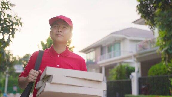 亚洲送货男工人穿着红色制服搬运食物披萨给年轻漂亮的女顾客在房前邮差和快递杂货配送服务理念