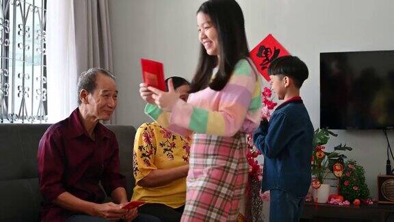 亚洲的孙子和孙女在中国新年期间在客厅问候和接受来自祖父母的春节红包(Angpow)