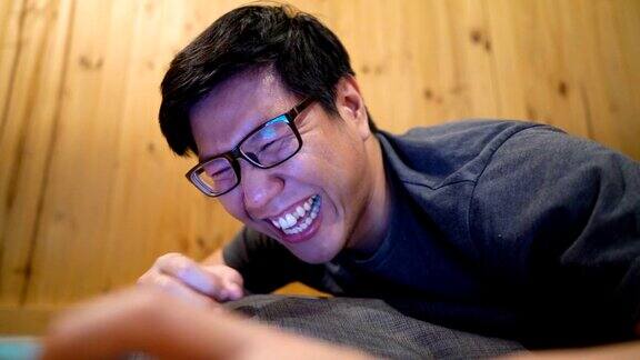 一名亚裔男子看着平板电脑屏幕笑得好厉害