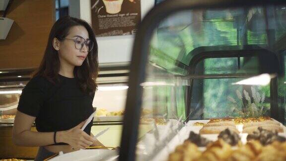 亚洲中国美女买糕点从一个咖啡馆选择拿着一个托盘