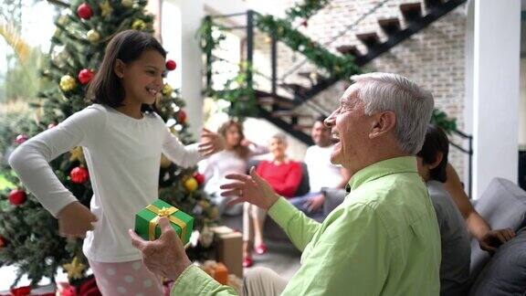 美丽的小女孩给爷爷一个圣诞礼物非常可爱的拥抱而家人坐在后面