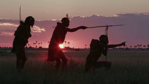 在博茨瓦纳的Makgadikgadi草原上夕阳下三名桑族人丛林人穿着传统服饰寻找动物的4K壮观的侧面画面