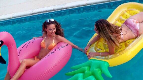 年轻的多民族女性朋友们在游泳池的夏季充气上漂浮