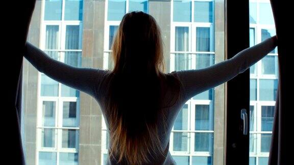 年轻女子拉开窗帘向窗外望去的剪影