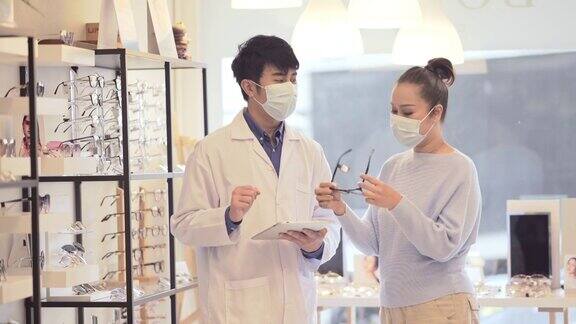 成熟女性戴防护口罩的患者在商店与眼科医生选择眼镜