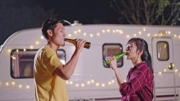 亚洲年轻男女旅行者朋友正在举行户外节日聚会夫妻俩一起喝一瓶啤酒晚上一起开怀大笑旅行自然露营车露营