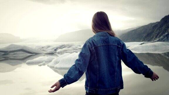 女孩在冰川泻湖在夕阳下张开双臂