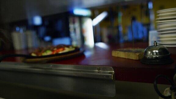 一名三十多岁的墨西哥男厨师将一盘热气腾腾的法士塔斯放在一家墨西哥餐厅的服务窗口并敲响了一个铃