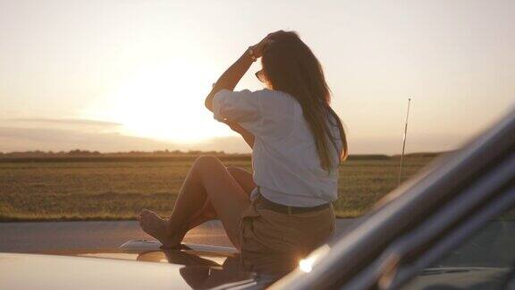 日落时分一名年轻女子坐在引擎盖上自拍