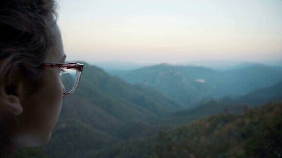 一个戴眼镜的小女孩站在悬崖边看着青山从后面看穿越群山