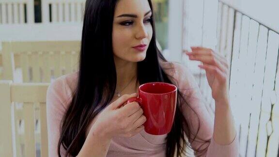 黑发女孩用红杯子喝热茶