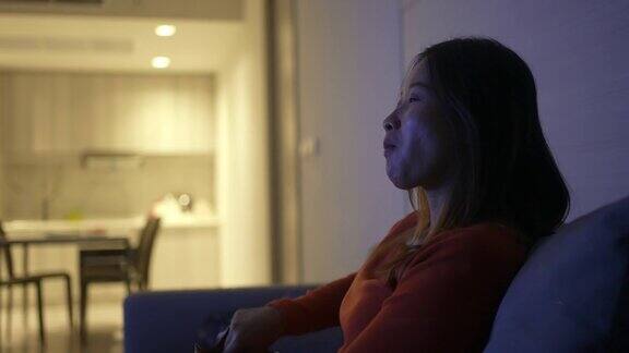 4K亚洲女人晚上坐在沙发上看电视吃着薯片