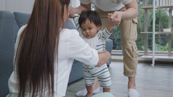 亚洲的儿子宝宝迈出了第一步走向他的母亲快乐的小婴儿在爸爸的帮助下学习走路并在家里教如何走路