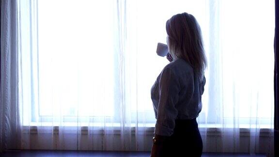 一位优雅的女孩站在窗边喝咖啡