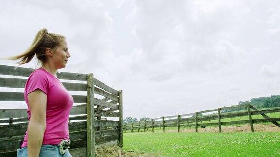 慢动作拍摄的一个年轻女子背着五加仑桶经过一个农场的马畜栏在一个部分阴天