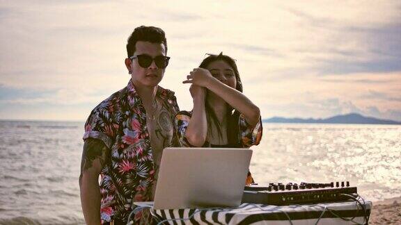 一对年轻夫妇在海滩上混音电子音乐