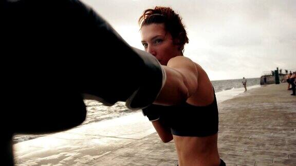 一个强壮的运动女性拳击手的特写镜头在一个袋子对着太阳在海边运动女拳击手训练Slowmotion拍摄