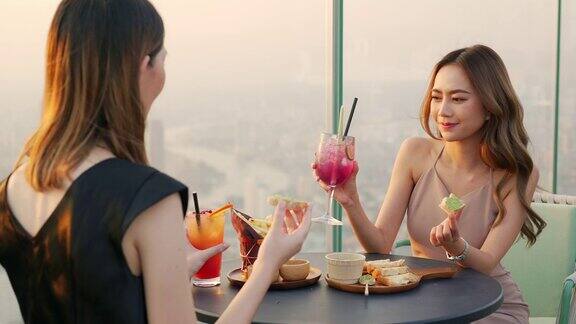 4K亚洲女性朋友在夏日夕阳下在摩天大楼的屋顶餐厅共进晚餐